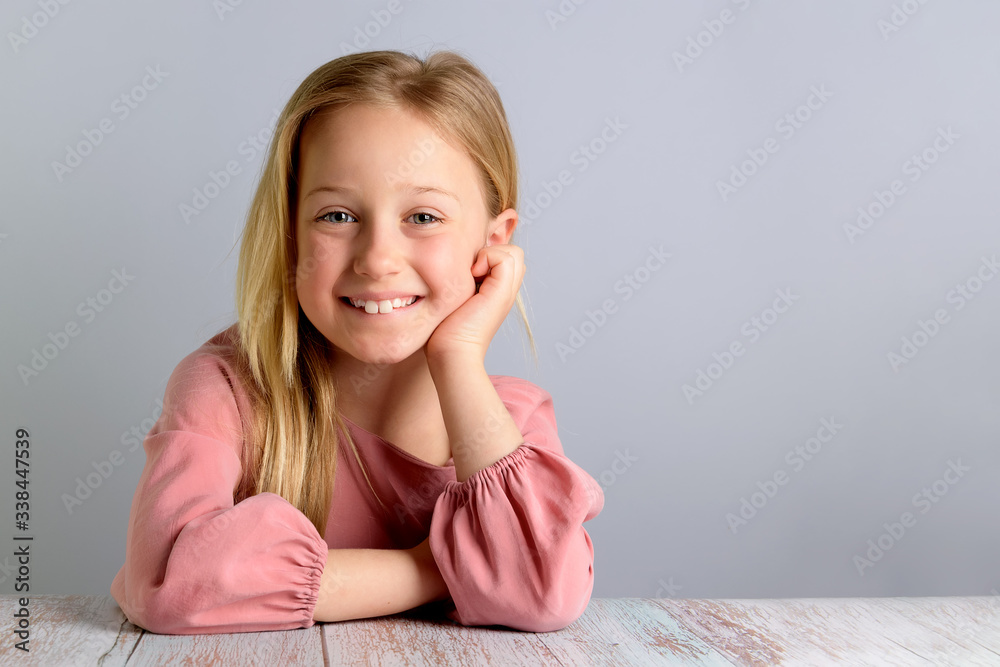 Portrait of a cute little girl in a pink dress posing in front of the camera. Smiling beautiful blonde with long hair on a gray background, copy space, headshot Portrait of a cute little girl in a pink dress posing in front of the camera. Smiling beautiful blonde with long hair on a gray background, copy space, headshot