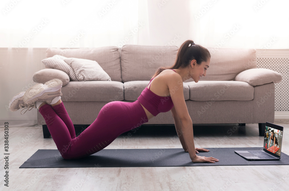 Online sport class. Young girl doing exercises, following video tutorial on laptop indoors Online sport class. Young girl doing exercises, following video tutorial on laptop indoors
