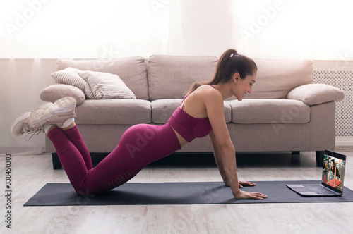 Online sport class. Young girl doing exercises, following video tutorial on laptop indoors