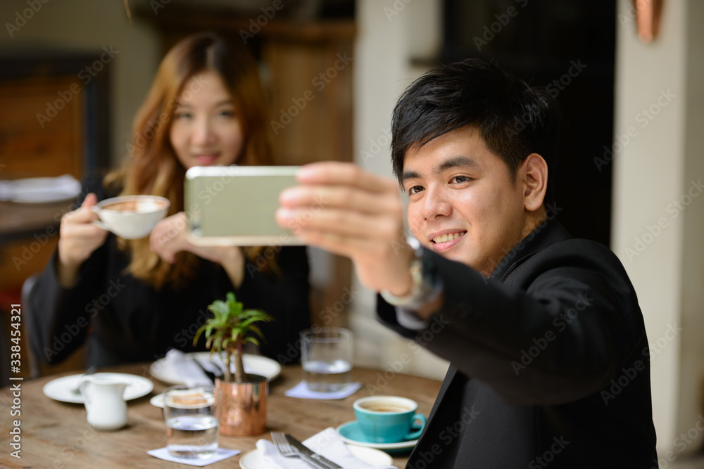Happy young Asian business couple taking selfie together at the coffee shop