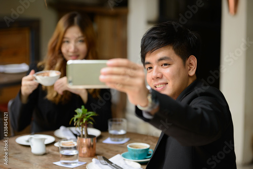 Happy young Asian business couple taking selfie together at the coffee shop