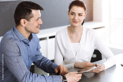 Friendly smiling businessman and woman working with computer in modern office. Headshot at meeting or workplace. Teamwork, partnership and business concept