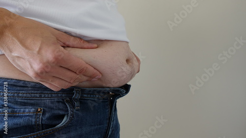 Man Squishing Belly Fat Standing On Left Side Wearing Jeans And White Shirt With Blank Background