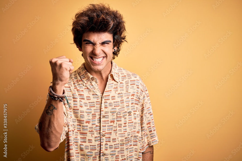 Young handsome man on vacation wearing summer shirt over isolated yellow background angry and mad raising fist frustrated and furious while shouting with anger. Rage and aggressive concept. Young handsome man on vacation wearing summer shirt over isolated yellow background angry and mad raising fist frustrated and furious while shouting with anger. Rage and aggressive concept.
