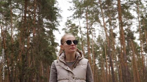 Beautiful woman in jacket waistcoat walk alone trailpath in pine forest in 4K photo