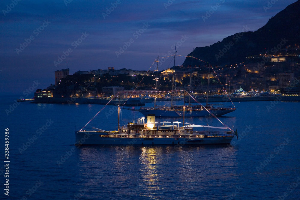 Yacht and seaside night view of Monte-Carlo with lights at dusk, in the Principality of Monaco, Western Europe on the Mediterranean Sea