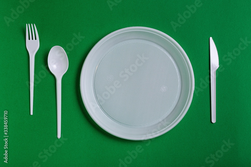 Plastic disposable utensils on green background. fork, knives, plates,