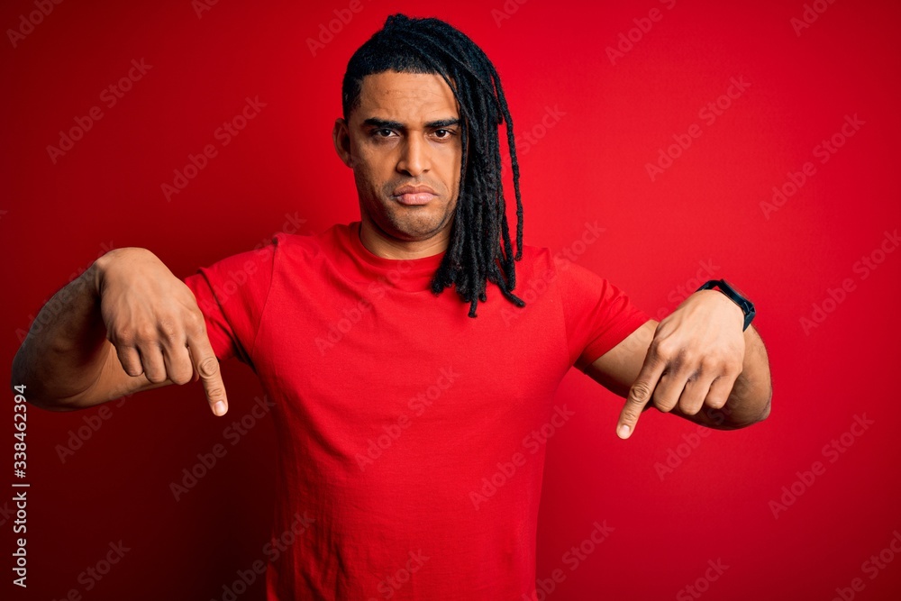 Young handsome african american afro man with dreadlocks wearing red casual t-shirt Pointing down looking sad and upset, indicating direction with fingers, unhappy and depressed. Young handsome african american afro man with dreadlocks wearing red casual t-shirt Pointing down looking sad and upset, indicating direction with fingers, unhappy and depressed.