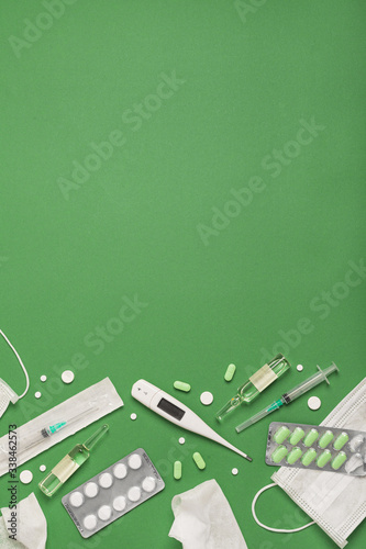 Medical masks, medicines, thermometer on a green background