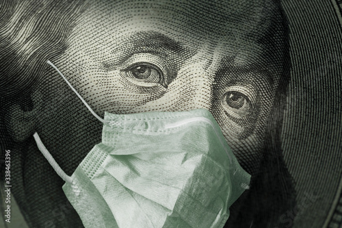 Portrait of Benjamin Franklin 100 dollar Bills with a medical mask from the coronavirus COVID-19.