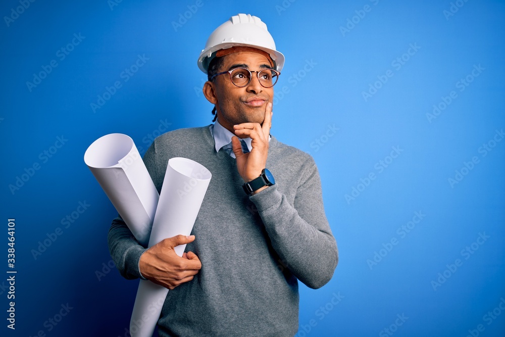 Young african american architect man wearing safety helmet holding bluprints serious face thinking about question, very confused idea Young african american architect man wearing safety helmet holding bluprints serious face thinking about question, very confused idea