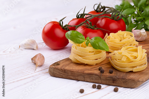 Raw tagliatelle pasta with fresh basil, garlic and tomatoes on a rustic white table