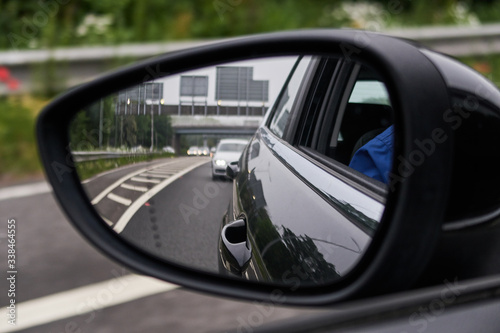 A rear view of a highway motorway, seen through the glass of a rear view mirror on an automobile car. Gloomy polluted city sky and vehicle backdrop. Driving a car fast on the city streets. © dannyburn