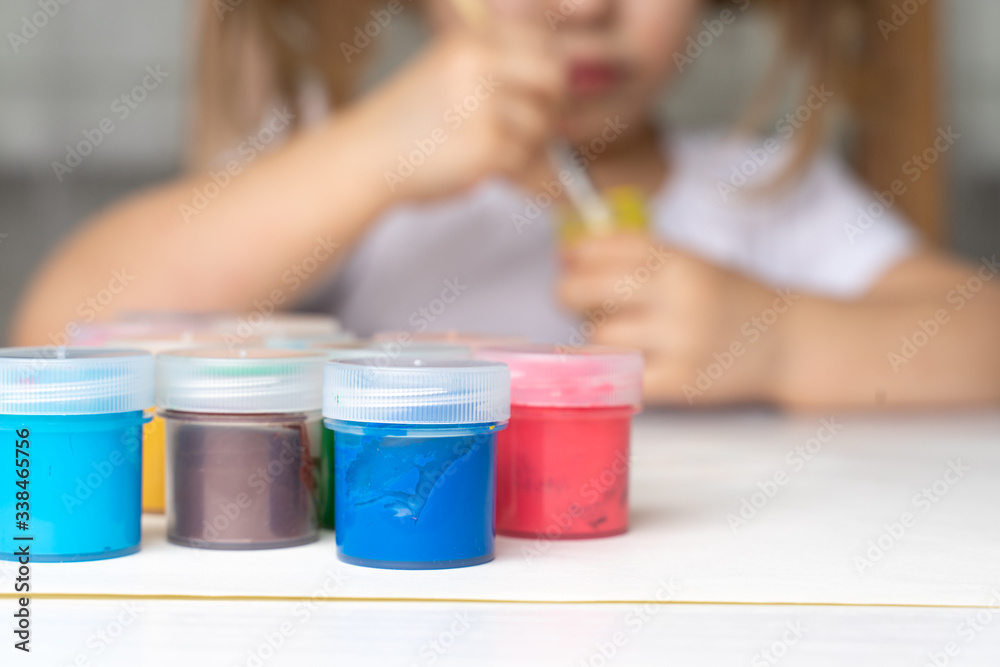 preparation for drawing paints, paints are different on the table. little girl soaks a brush in yellow paint preparation for drawing paints, paints are different on the table. little girl soaks a brush in yellow paint