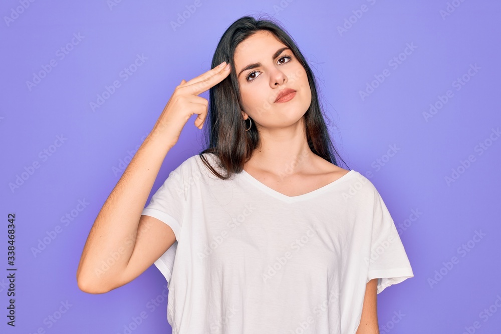 Young beautiful brunette woman wearing casual white t-shirt over purple background Shooting and killing oneself pointing hand and fingers to head like gun, suicide gesture. Young beautiful brunette woman wearing casual white t-shirt over purple background Shooting and killing oneself pointing hand and fingers to head like gun, suicide gesture.
