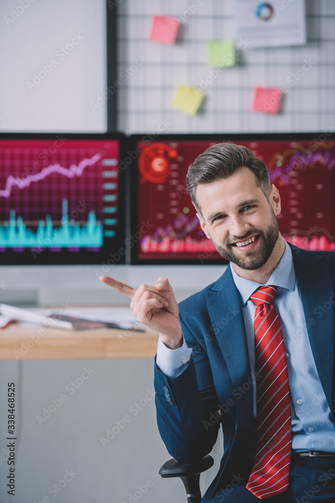 Smiling information security analyst pointing with finger near computers on table in office Smiling information security analyst pointing with finger near computers on table in office