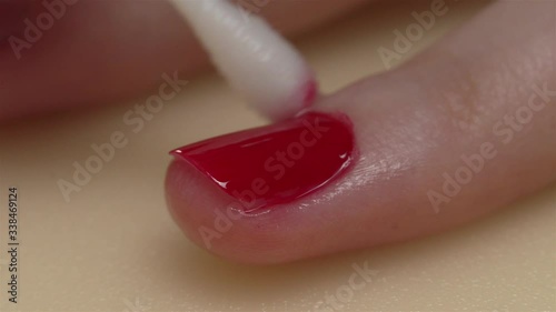 Macro shot with manicure, a woman paints her nails in red, makeup and nails, removes excess paint with a cotton swab. closes the application of nail polish. photo
