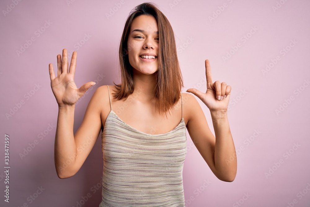 Young beautiful brunette girl wearing casual striped t-shirt over isolated pink background showing and pointing up with fingers number seven while smiling confident and happy. Young beautiful brunette girl wearing casual striped t-shirt over isolated pink background showing and pointing up with fingers number seven while smiling confident and happy.