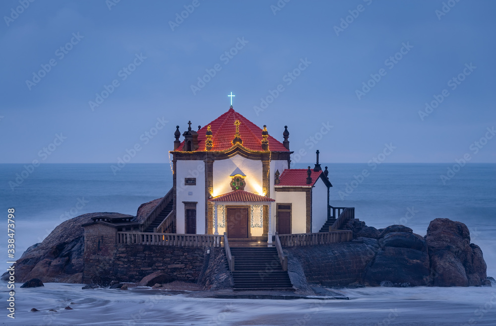 Beautiful church at the beach. Capela Senhor da Pedra, at sunset, with waves crashing over the church