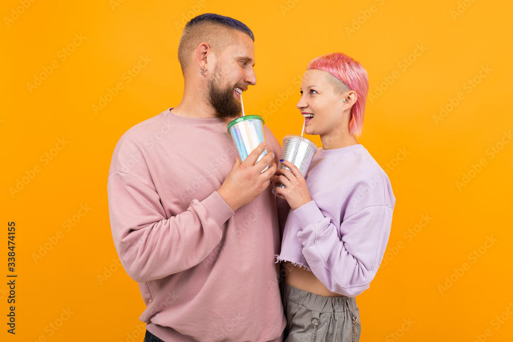 Unusual pretty woman with short pink hair and tattoo drinks coffee and having fun with her boyfriend isolated on orange background Unusual pretty woman with short pink hair and tattoo drinks coffee and having fun with her boyfriend isolated on orange background