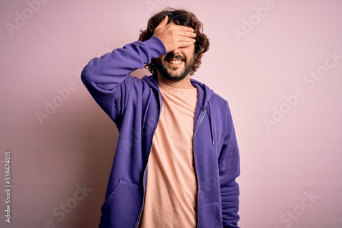 Young handsome sporty man with beard wearing casual sweatshirt over pink background smiling and laughing with hand on face covering eyes for surprise. Blind concept. © Krakenimages.com