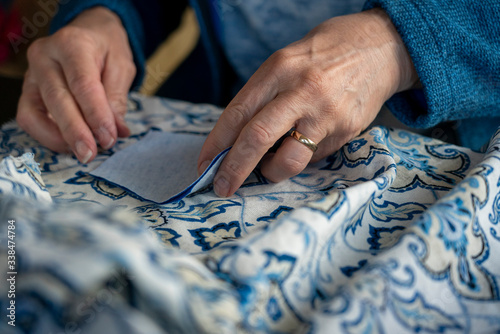 A closeup photo shows a seamstress laying out the fabric pattern for a homemade covid-19 coronavirus protection mask.