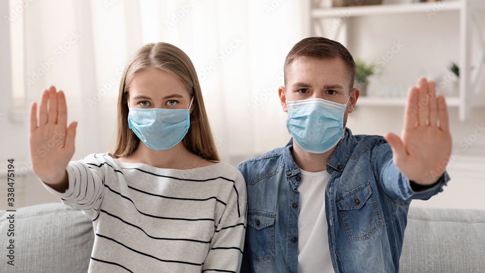 Young couple in protecting masks gesturing STOP at home