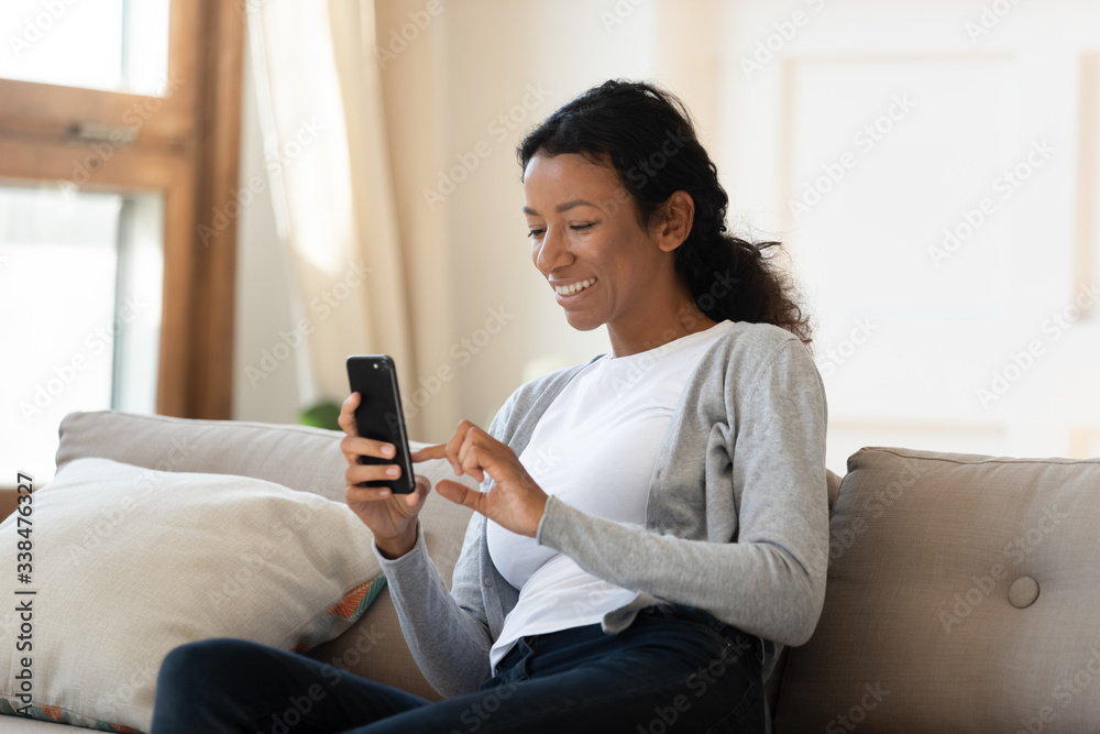 African american smiling woman sit on couch, hold smartphone in her ...