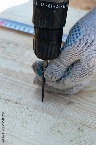 Screw the screw with an electric screwdriver into a wooden board, close-up