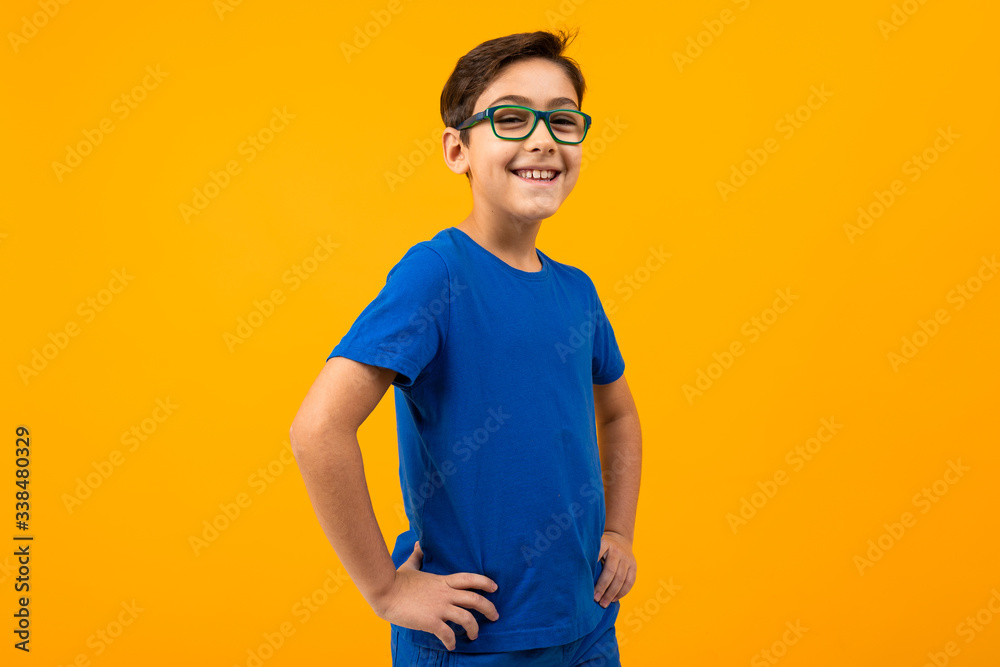 boy in a blue T-shirt with glasses posing on a yellow background with ...