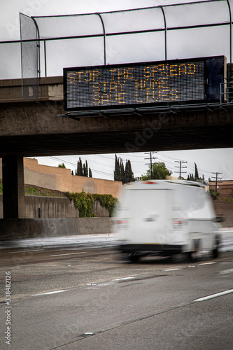 Government digital freeeway sign at overpass with message stating “Stop The Spread ,Stay Home, Save Lives” and traffic blurred under the sign during the Coronavirus Pandemic photo