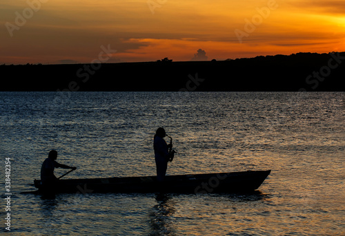 Fototapeta Naklejka Na Ścianę i Meble -  Sax played from inside a boat, during sunset . Jacaré River, Brazil.