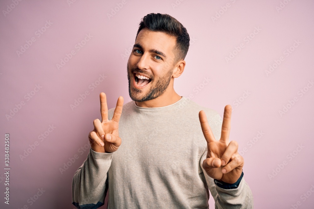 Young handsome man wearing casual sweater standing over isolated pink background smiling looking to the camera showing fingers doing victory sign. Number two. Young handsome man wearing casual sweater standing over isolated pink background smiling looking to the camera showing fingers doing victory sign. Number two.