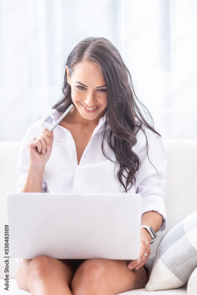 Portrait of a seductive looking young female holding a pen in hand close to her face sitting dressed only in her white shirt in her bright living room, looking into a notebook on her knees Portrait of a seductive looking young female holding a pen in hand close to her face sitting dressed only in her white shirt in her bright living room, looking into a notebook on her knees