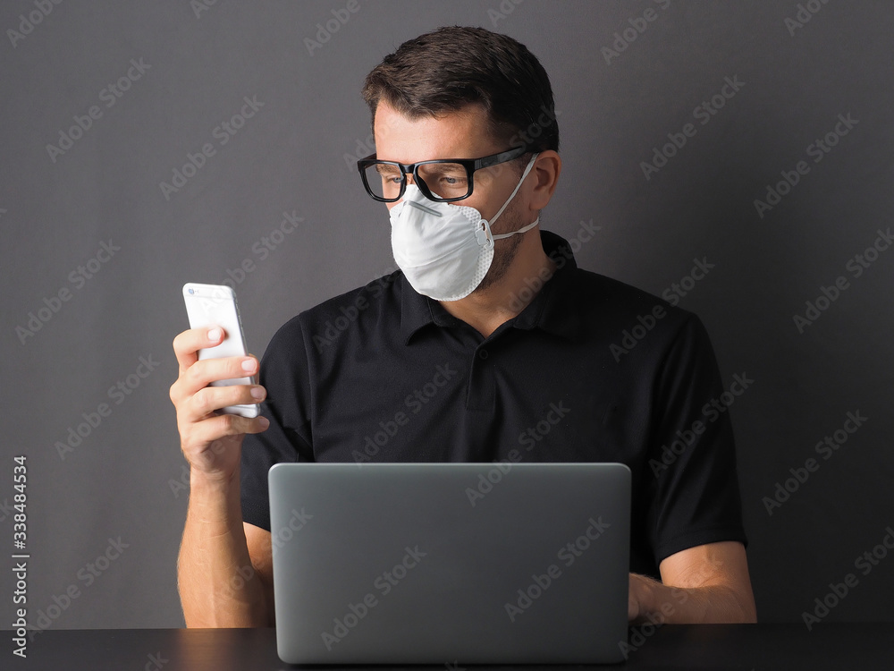Portrait of a man working in home with laptop and phone with protective mask on his face. Coronavirus disease (Covid19) awareness. People protect from Covid-19 or 2019 nCoV. Portrait of a man working in home with laptop and phone with protective mask on his face. Coronavirus disease (Covid19) awareness. People protect from Covid-19 or 2019 nCoV.