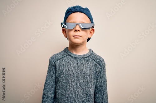 Young little caucasian kid wearing internet meme thug life glasses over isolated background with serious expression on face. Simple and natural looking at the camera.