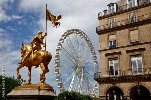 A statue of Joan of Arc stands in the Place des Victoires with a large ferris wheel in the Tuileries Gardens, Paris France - shot July 24, 2015