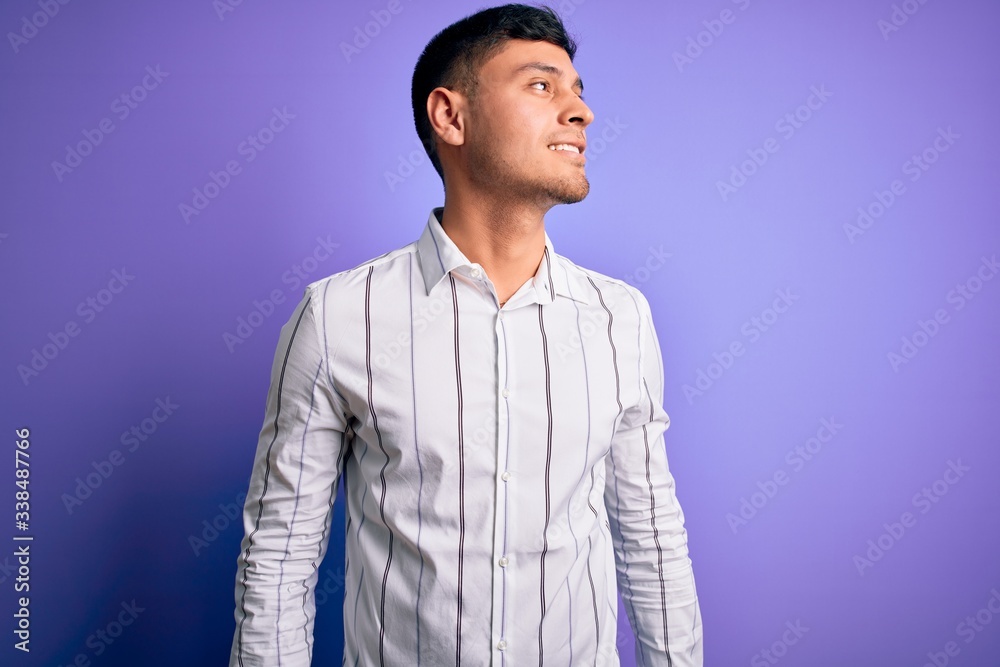 Young handsome hispanic man wearing elegant business shirt standing over purple background looking away to side with smile on face, natural expression. Laughing confident. Young handsome hispanic man wearing elegant business shirt standing over purple background looking away to side with smile on face, natural expression. Laughing confident.