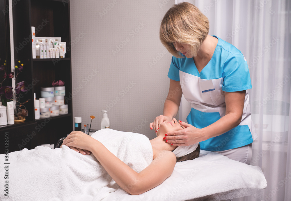Young woman is enjoying facial procedure at beauty salon. Girl is lying in spa and getting face massage with pleasure Young woman is enjoying facial procedure at beauty salon. Girl is lying in spa and getting face massage with pleasure