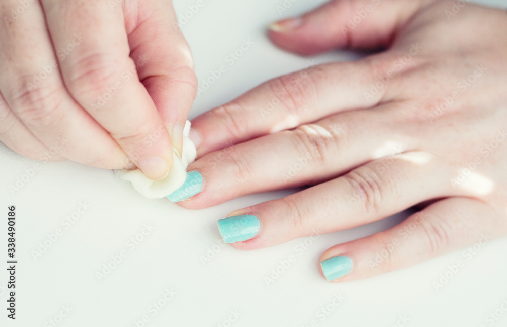 Removing nail Polish at home. Woman removes the nail polish. Hands with blue manicure on whote table. Removing nail Polish at home. Woman removes the nail polish. Hands with blue manicure on whote table.