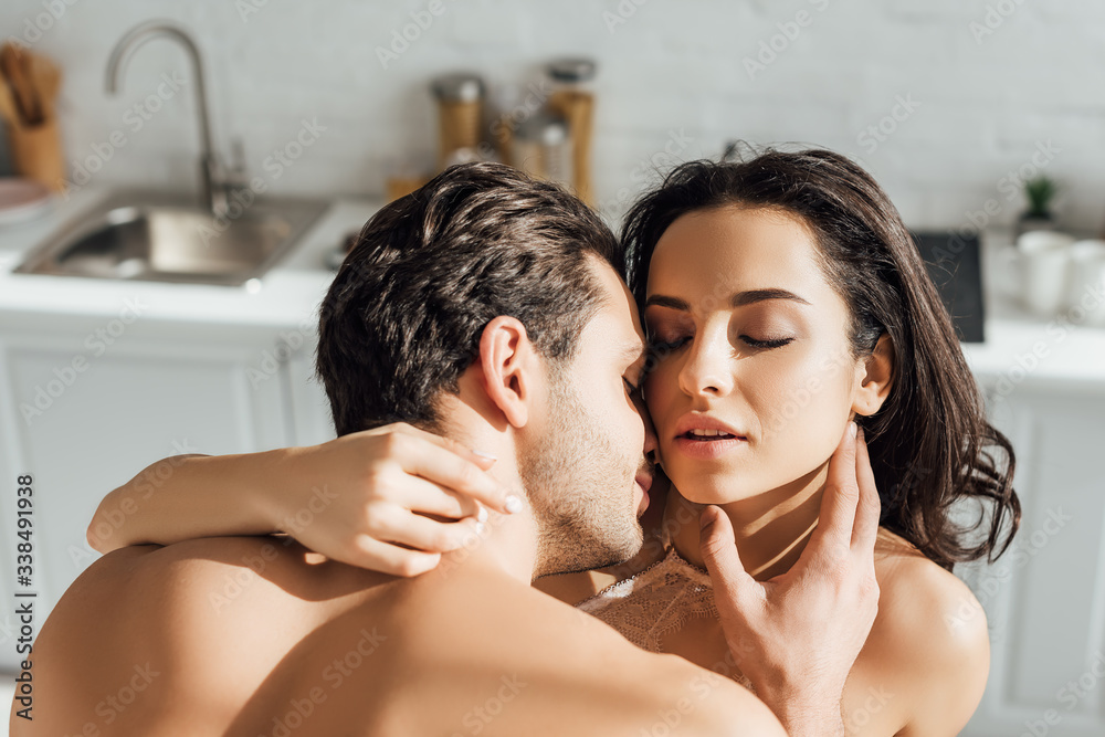 Fototapeta premium Passionate woman and man with closed eyes hugging in kitchen