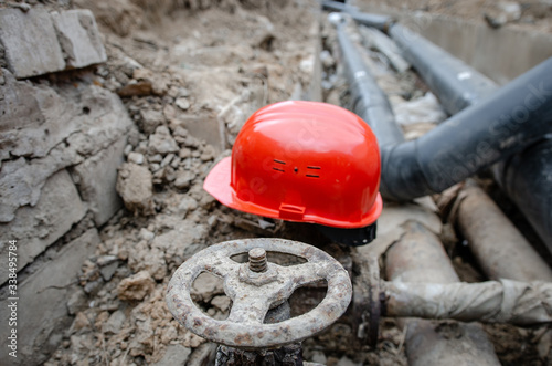  Rusty valve on the pipeline. Safety orange helmet and valve on the heating main. Outdated clinker valve on the municipal heat pipe. repair of the heating main damaged section, an emergency photo