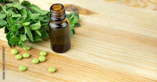 Peppermint oil in a glass bottle with fresh mint leaves on a wooden table. Copy space.