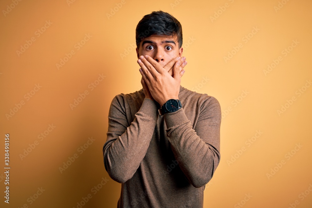 Young handsome man wearing casual turtleneck sweater over isolated yellow background shocked covering mouth with hands for mistake. Secret concept.