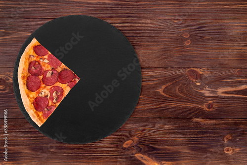 A slice of salami pizza with mushrooms, on slate bottom, on wooden table top view, space for text
