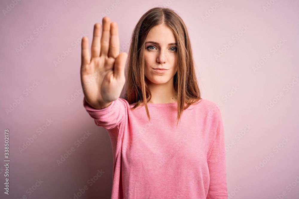 Young beautiful redhead woman wearing casual sweater over isolated pink background doing stop sing with palm of the hand. Warning expression with negative and serious gesture on the face. Young beautiful redhead woman wearing casual sweater over isolated pink background doing stop sing with palm of the hand. Warning expression with negative and serious gesture on the face.