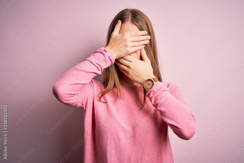 Young beautiful redhead woman wearing casual sweater over isolated pink background Covering eyes and mouth with hands, surprised and shocked. Hiding emotion Young beautiful redhead woman wearing casual sweater over isolated pink background Covering eyes and mouth with hands, surprised and shocked. Hiding emotion