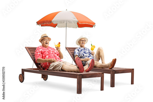 Fotografia Two senior male tourist with cocktails lying on sunbeds with an umbrella