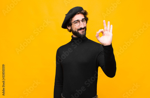 young french artist man feeling happy, relaxed and satisfied, showing approval with okay gesture, smiling against orange wall photo