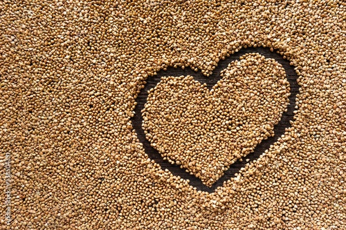 flat surface covered with brown buckwheat with a heart in it pictured from above